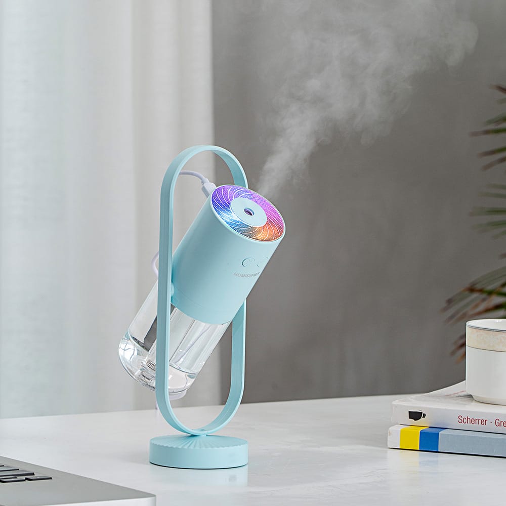Portable mint green smart aroma diffuser and mist humidifier displaying dynamic light on a white desk.